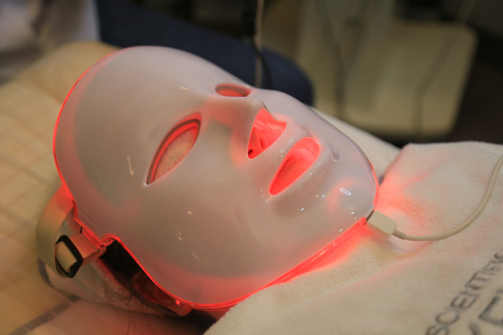 Mujer usando la máscara LED de terapia facial Tibia con luz roja durante una sesión en casa